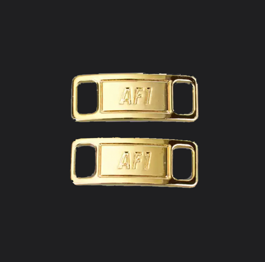 The image is featuring a pair of gold shoe tags on a blank black background. The air force 1 shoes tags are for sneaker laces and come in pairs. 