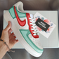 The image is of a Custom Nike Air Force 1 sneaker on a shoe box background. The custom sneakers are painted in lighter blue and red colors with shadings.