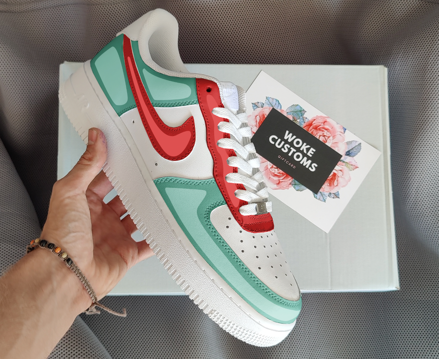 The image is of a Custom Nike Air Force 1 sneaker on a shoe box background. The custom sneakers are painted in lighter blue and red colors with shadings.