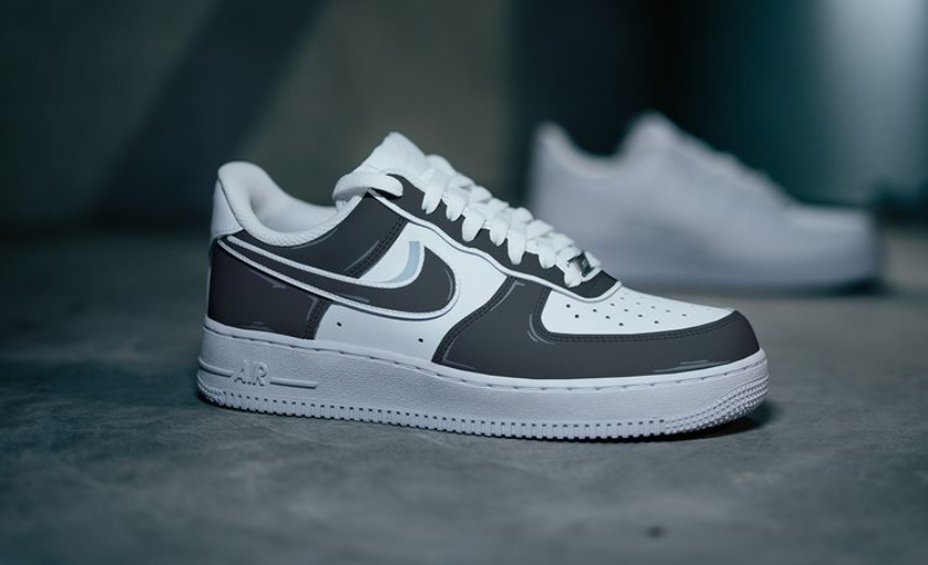 The image is of a Custom Nike Air force 1 sneaker pair on a gray street background. The white custom sneakers have a black cartoon styled design. 