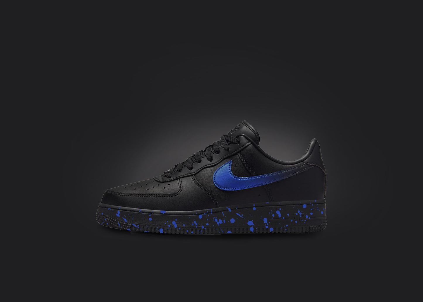 The image is featuring a custom black Air force 1 sneaker on a blank black background. The black nike sneaker has a blue paint splatter design on the sole and a blue fade on the nike logo.